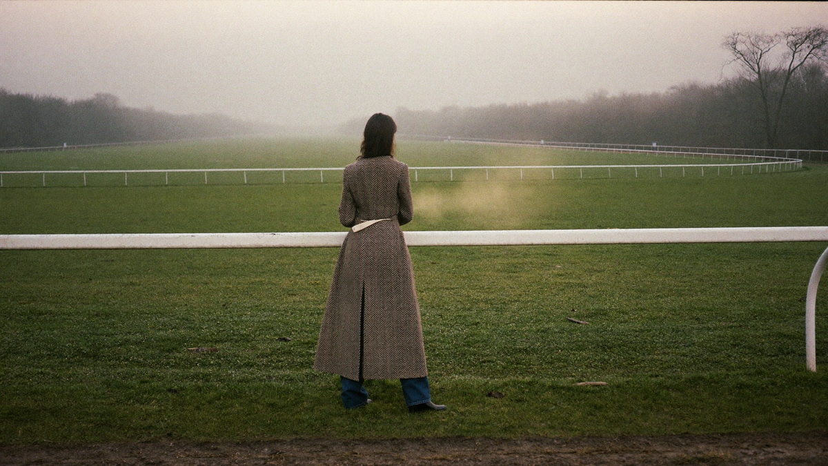 A woman in a long herringbone tweed riding jacket at a misty Gloucestershire racecourse in November - the winter racing wardrobe