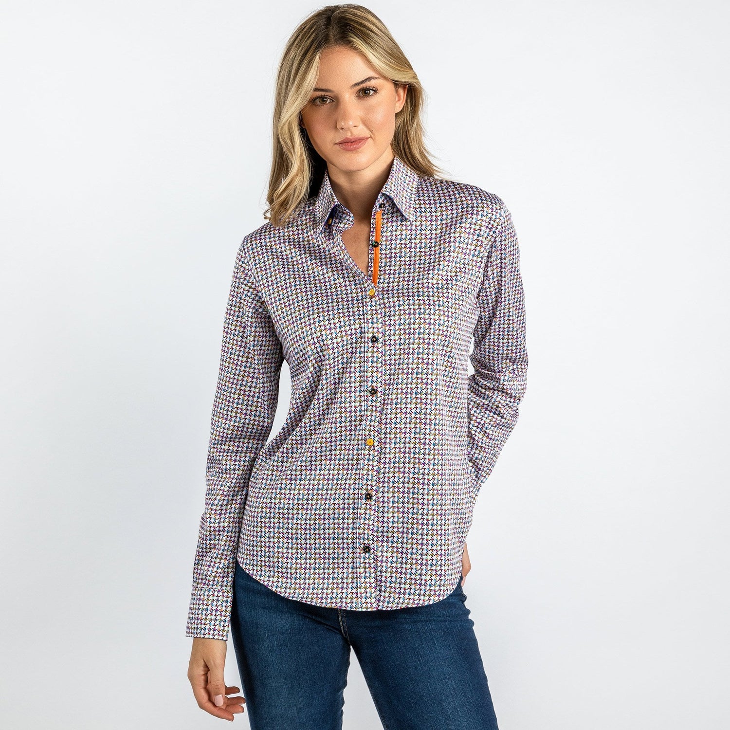 Woman wearing a vibrant multicolour houndstooth printed shirt made of satin-cotton blend, styled with blue jeans against a white background.