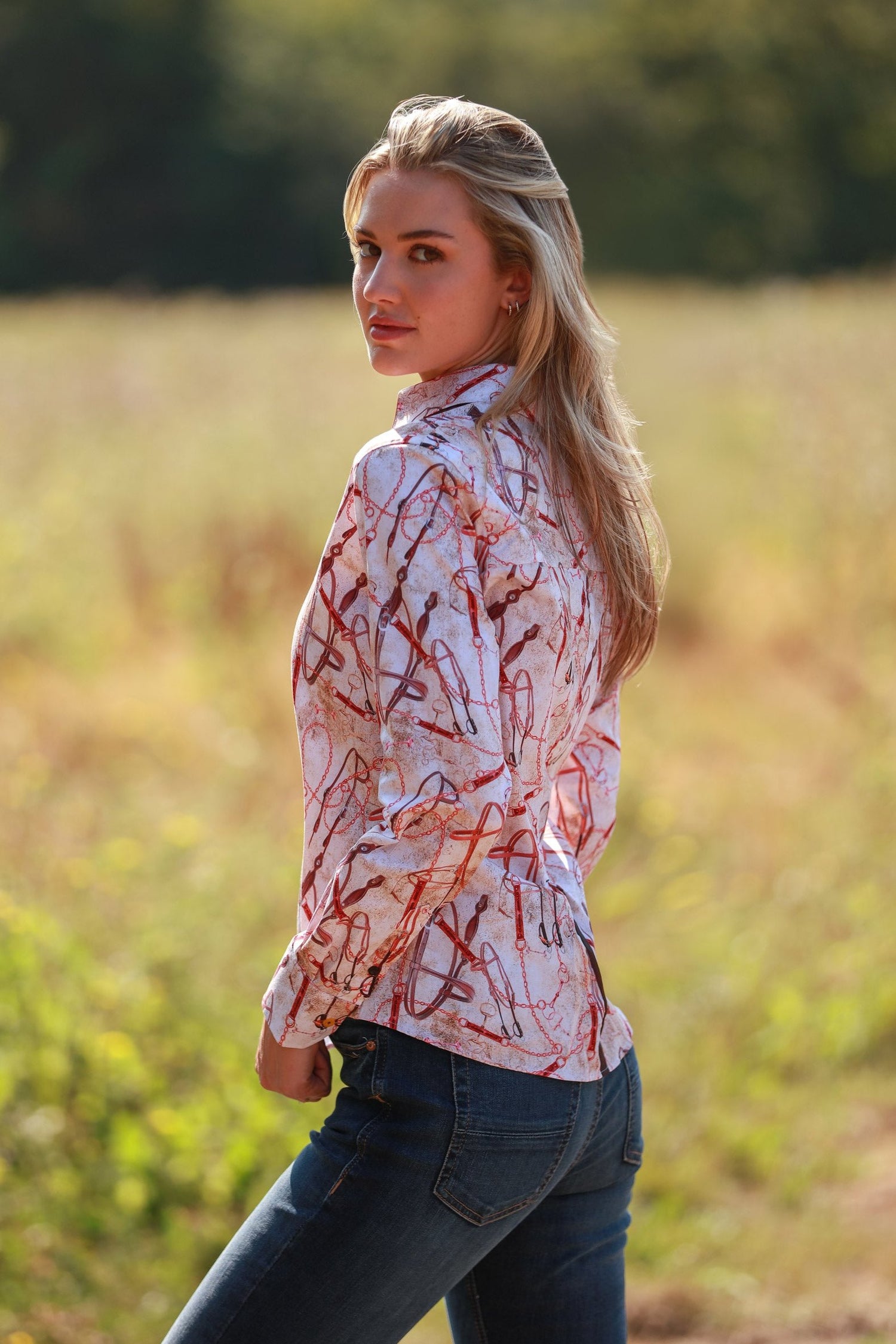 Woman wearing Snaffle print shirt in countryside, showcasing equestrian-inspired fashion with intricate snaffle bit design.