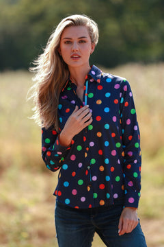 Woman wearing multicolour polkadot print shirt, standing outdoors in casual jeans.