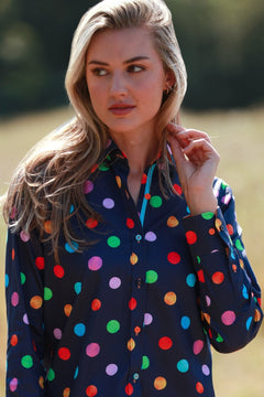 Woman wearing a vibrant multicolour polkadot print shirt in a field, showcasing casual and playful fashion style