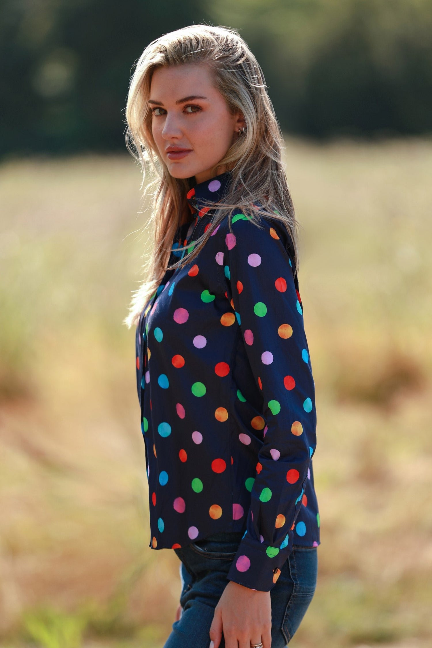 Woman wearing a vibrant multicolour polkadot print shirt in a natural outdoor setting.