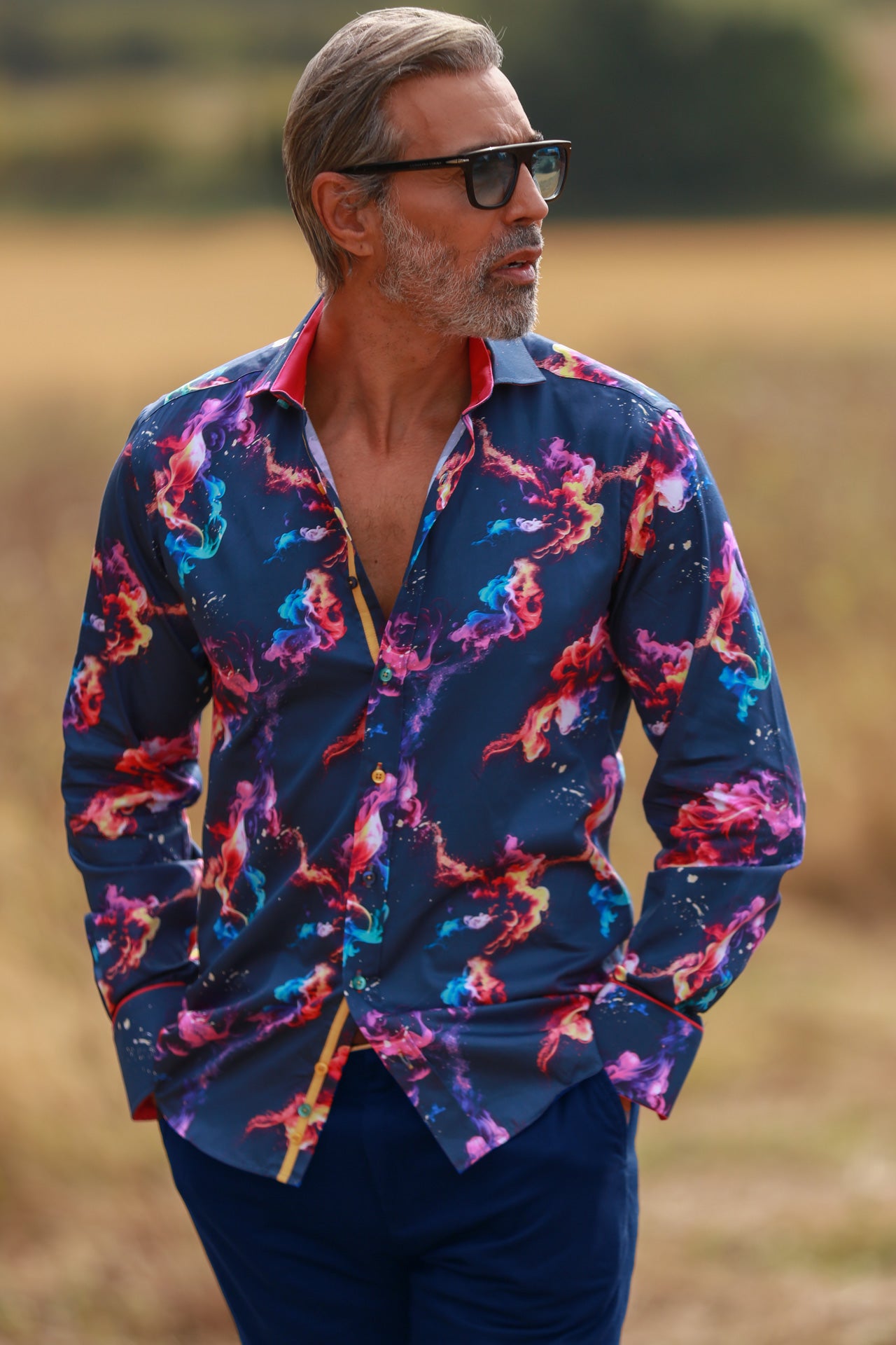 Man wearing SMOKE MULTICOLOUR PRINT SHIRT with vibrant hues and hot fuchsia inserts and cuffs, standing outdoors.