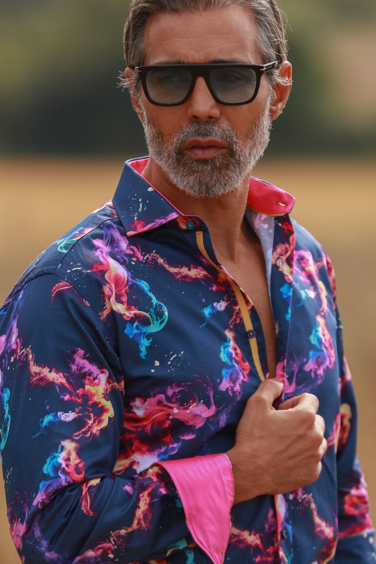 Man wearing SMOKE MULTICOLOUR PRINT SHIRT with vibrant swirls on navy background, hot fuchsia inserts, and cuffs, outdoors.