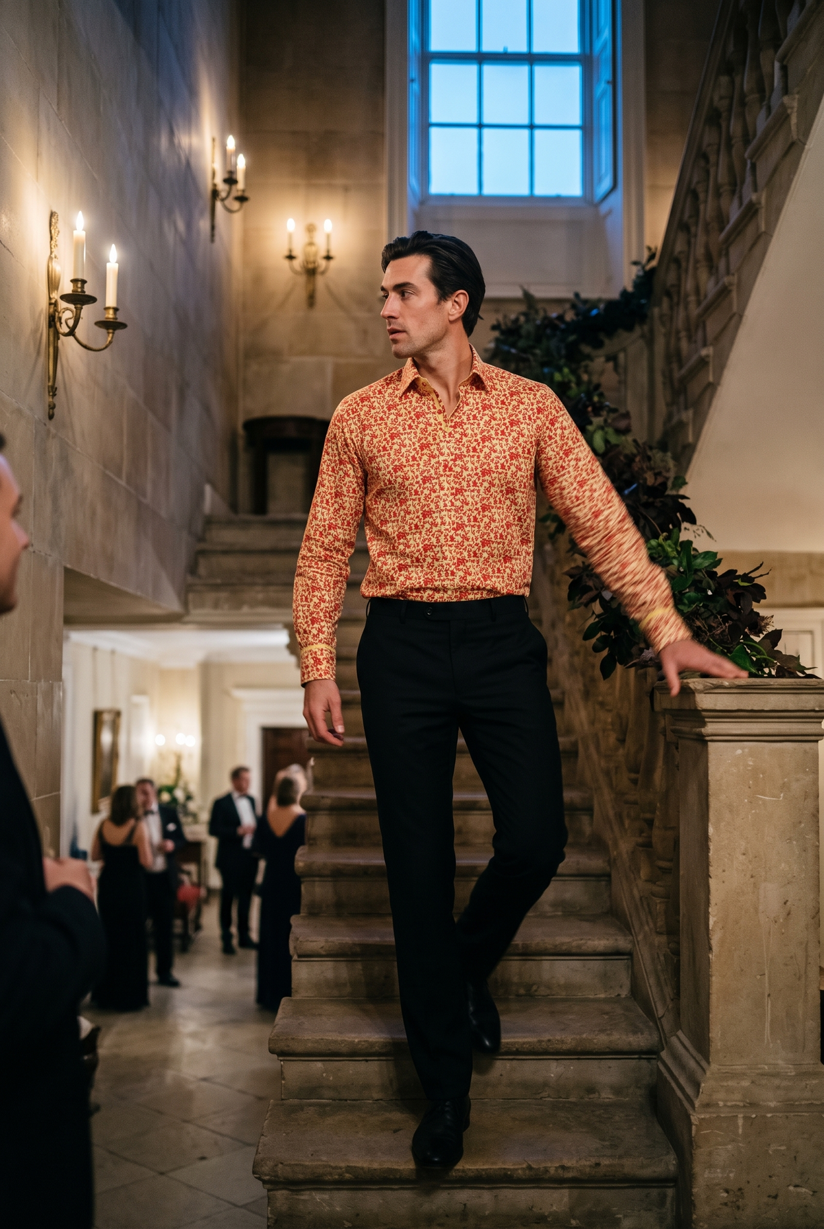 A man in his late twenties wearing a Claudio Lugli Baroque Legacy Collection print shirt at a black tie evening, coming down the stone staircase of Georgian assembly rooms past candle sconces, the cream ground and scattered red motifs reading clearly