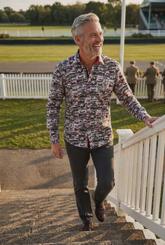 A man walks up the grandstand steps at a vintage motor racing meeting wearing the Claudio Lugli Vintage Race Car print shirt, a collage of black and white racing photographs on premium satin cotton